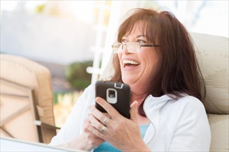 Attractive middle aged woman laughing while using her smart phone on the patio