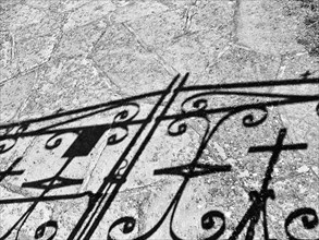 Wrought iron gate with cross casting shadows on a path