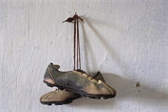 Hanging old leather football boots on nail in front of white wall