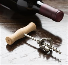 Abstract wine bottle and corkscrew laying on a reflective wood surface