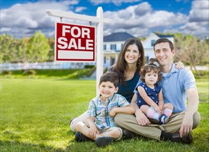 Young family with children in front of custom home and for sale real estate sign