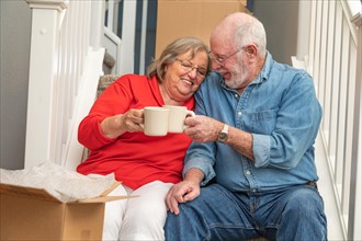 Tired senior adult couple resting on stairs with cups of coffee surrounded with moving boxes