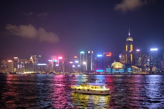 Hong Kong skyline cityscape downtown skyscrapers over Victoria Harbour in the evening illuminated with tourist boat ferries