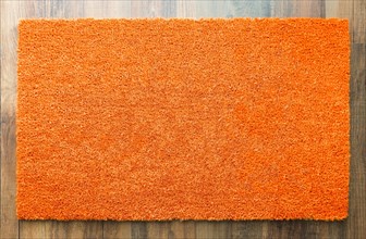 Blank orange welcome mat on wood floor background ready for your own text