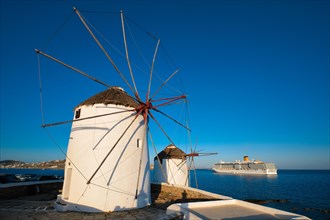 Scenic view of famous Mykonos town windmills. Traditional greek windmills on Mykonos island at sunrise with cruise ship in background