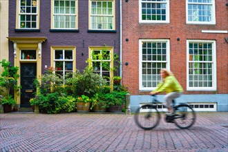 Motion blurred bicycle rider cyclist woman on bicycle very popular means of transport in Netherlands in street with old houses of Delft