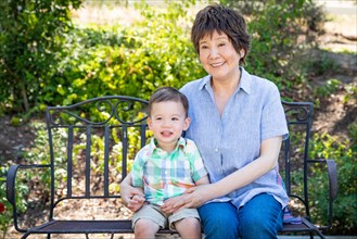 Chinese grandmother and mixed-race child sit on bench outdoors