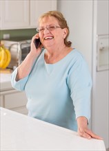 Happy senior adult woman on her smart cell phone in kitchen