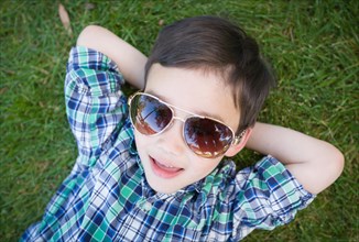 mixed-race chinese and caucasian young boy wearing sunglasses relaxing on his back outside on the grass