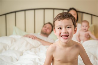 Young mixed-race chinese and caucasian boy laying in bed with his family