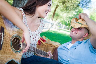 Young adult girl playing guitar with boyfriend in the park