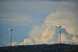 Wind turbines standing on a little Hill in front of a huge cloud