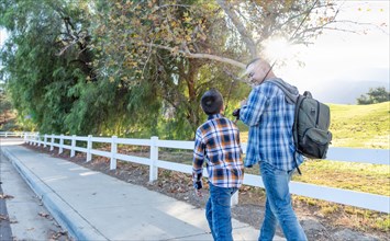 mixed-race father and son outdoors walking with fishing poles