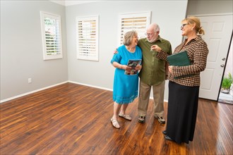 Female real estate agent handing new house keys to senior adult couple in new home