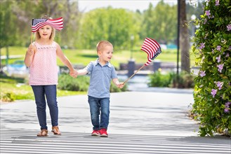 Young sister and brother waving american flags at the park