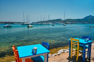 Cafe restaurant table of street cafe with chairs on beach in Adamantas town on Milos island with Aegean sea with boats and yachts in background. Milos island