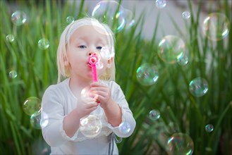 Adorable little girl sitting on bench having fun with blowing bubbles outside