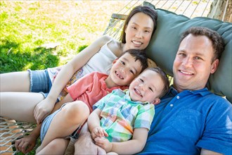 Caucasian father and chinese mother relaxing in hammock with mixed-race sons