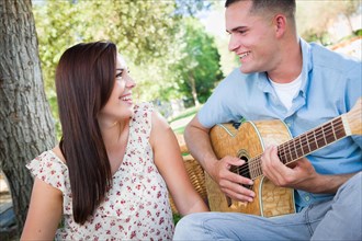 Young adult man playing guitar for his girlfriend in the park