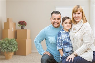 Happy mixed-race family with son in room with packed moving boxes