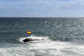 A Spanish flag on rocks in the Atlantic Ocean during windy weather in Pozo Izquierdo Bay