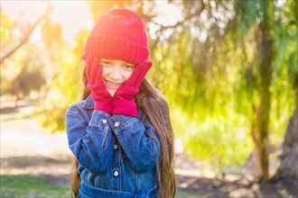 Cute mixed-race young girl wearing red knit cap and mittens outdoors