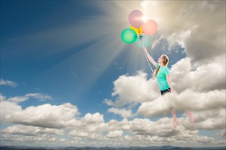 Young adult female being carried up and away into the clouds by balloons that she is holding