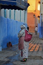 Woman with shopping bag on her back standing in alley with evening light