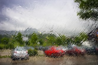Blick durch eine nasse Windschutzscheibe auf geparkte Autos am Parkplatz