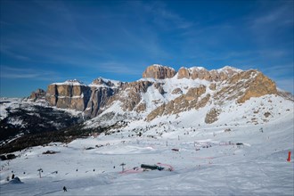 View of a ski resort piste with people skiing in Dolomites in Italy. Ski area Belvedere. Canazei