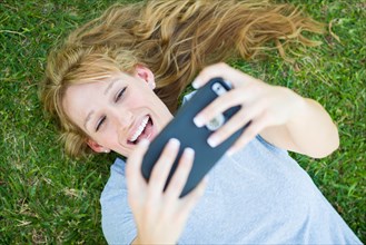 Young adult woman laying in grass taking a selfie with her smart phone