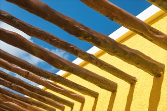 Abstract wood post beams and bright yellow wall against blue sky