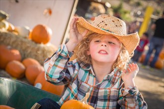 Little boy sitting with A cowboy hat in a rustic ranch setting at the pumpkin patch