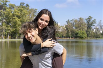 Young couple at a lake. Boyfriend carrying his girlfriend on piggyback. Funny and happy expression