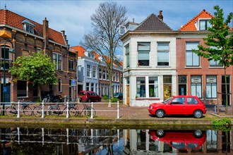 Cars and bicycles on canal embankment in street of Delft with reflection. Delft