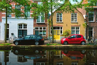 Cars and bicycles on canal embankment in street of Delft with reflection
