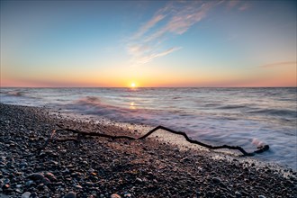 Langzeitbelichtung von einem Ast am Strand der Ostsee bei Sonnenuntergang und starkem Wellengang