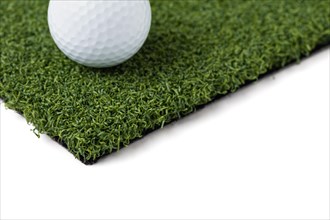 Golf ball resting on section of artificial turf grass on white background