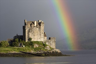 View of restored castle on tidal island in sea loch with rainbow