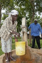 Woman filling buckets with clear water at the well of a hand pump in the village