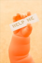 Toy doll hand holding paper with HELP ME wording
