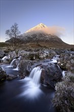 View of moorland with small waterfalls in rocky stream and snow-capped mountain in background at dawn