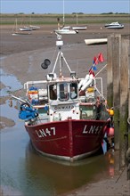 Fishing boat moored at jetty in coastal creek at low tide
