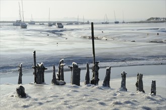 View of ice-covered mudflats and salt marshes with old jetty and sailing boats in the distance