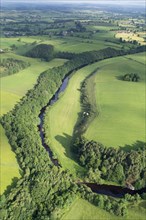 Aerial view of river lined with native woodland flowing through the countryside
