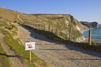View of coastal footpath and sign warning of 45 degree gradient for walkers