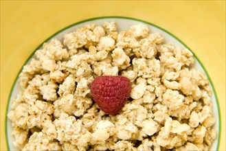 Granola cereal with raspberry in a yellow bowl