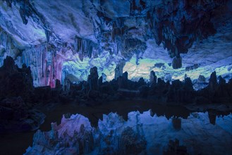 Interior of a limestone cave with stalactites and stalagmites reflected in a pond