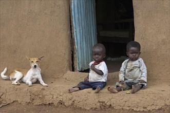 Malnourished toddlers in poor clothes sitting outside the house with dog