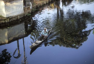 A fisherman rowing a sailboat using a stick in backwaters of kerala
